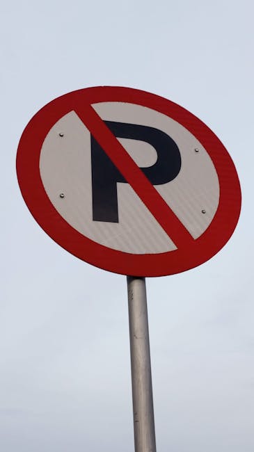 A circular traffic sign with a white background, a bold black letter 'P', and a red diagonal line crossing through it, indicating no parking. The sign is mounted on a slim metal pole and is set against a plain, overcast grey sky. The sign is positioned near the entrance to a residential property, which may be relevant for house removals or large furniture transport. The image appears to be related to parking restrictions during home relocation or moving services, as referenced in the context of Ilford parking suspension rules for removals on the company's website, removalsilford.org.uk.